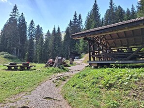 Shaded picnic area with a rustic shelter and benches amidst a lush landscape.