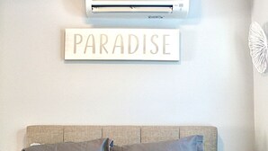 A bedroom with a bed, a wall-mounted air conditioner, and a sign that reads "PARADISE". - A beautiful tiny house in a beautiful little paradise for you to enjoy nature (Ocean Isle Beach)
