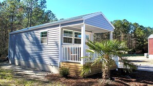 A small, single-story mobile home with a front porch and a palm tree in the yard. - A beautiful tiny house in a beautiful little paradise for you to enjoy nature (Ocean Isle Beach)