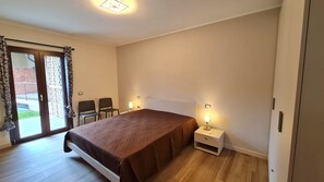 Een slaapkamer met een bed, twee stoelen, een nachtkastje met een lamp en een schuifdeur naar buiten.