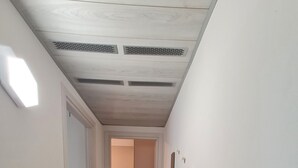 Un pasillo estrecho con suelo de madera, paredes blancas y un radiador blanco a la derecha. Se ve una lavadora en la esquina izquierda.
