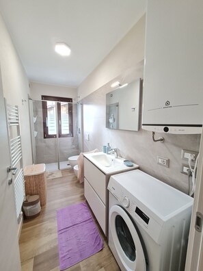 Een kleine, moderne badkamer met douche, toilet, wastafel en een wasmachine.