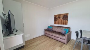 Een compacte, moderne woonkamer met een bank, een schilderij en een televisie.