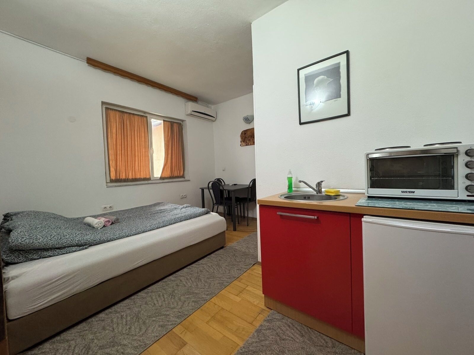 Una stanza compatta con un letto, angolo cottura, zona pranzo e finestra con tende.