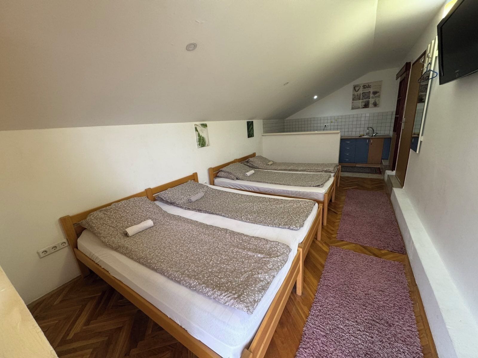 Quarto de dormitório com três camas de madeira, uma cozinha compacta e um chão de madeira com padrão herringbone.