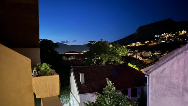 A nighttime view of a hillside town with buildings illuminated against a dark sky. - Villa Anja Apartments (Mostar)