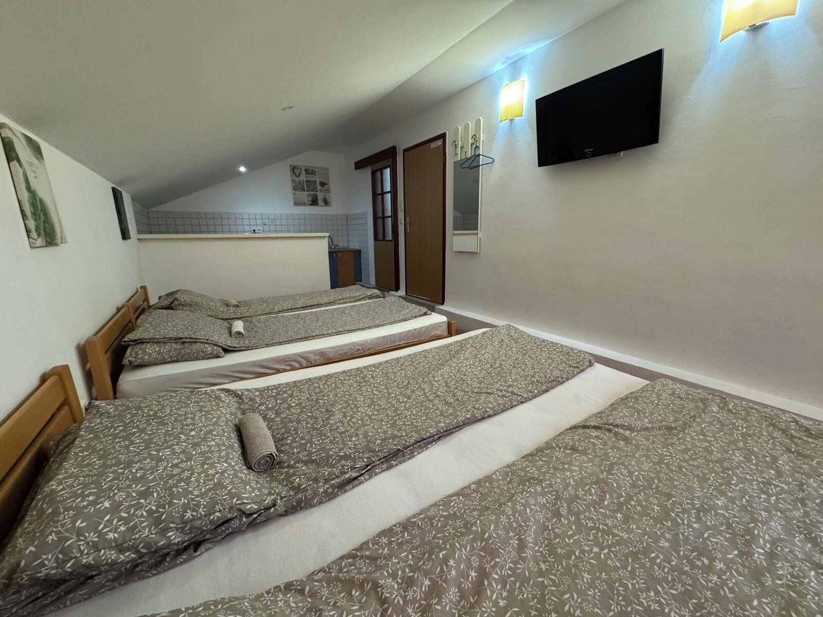 Een kamer met drie bedden, een aan de muur bevestigde televisie en een klein kitchenette.
