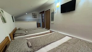 A room with three beds arranged in a row, a television mounted on the wall, and a small kitchenette area in the background. - Villa Anja Apartments (Mostar)