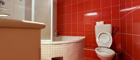 Une salle de bain avec des murs recouverts de carreaux rouges, des toilettes blanches et une baignoire.