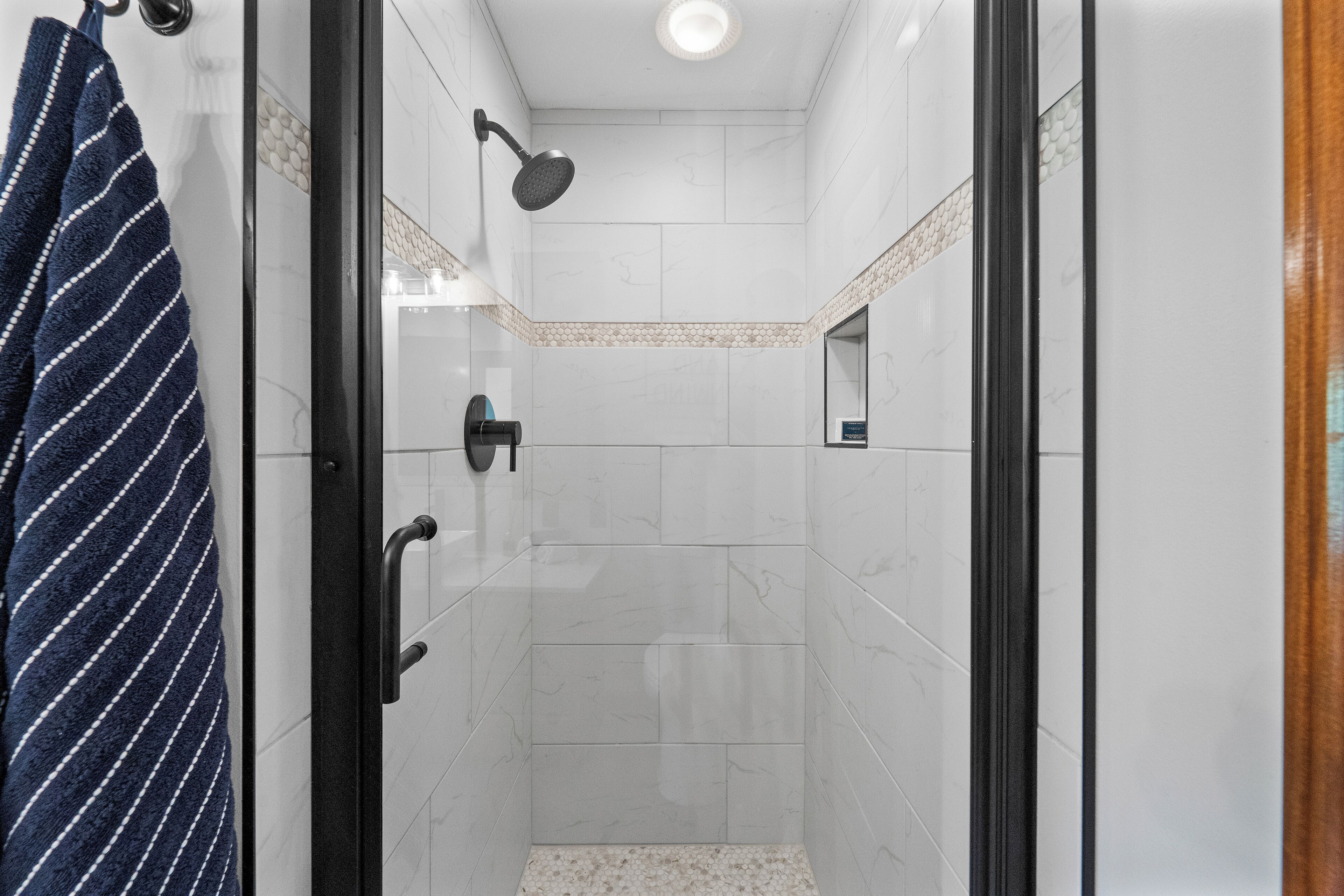 A shower area with a glass door, a towel rack with a striped towel, and a tiled floor.