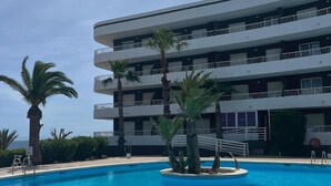 A multi-story hotel with a swimming pool surrounded by palm trees. - Palmera Beach by Renthas (Orihuela)