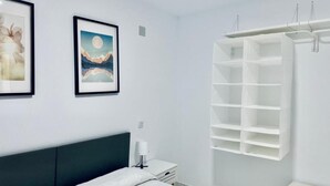 A bedroom with a bed, a nightstand, a wall-mounted shelf, and two framed pictures. - Palmera Beach by Renthas (Orihuela)