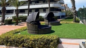 A modern multi-story hotel with balconies, palm trees, and outdoor seating areas. - Palmera Beach by Renthas (Orihuela)