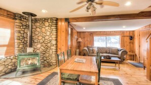 Interior acogedor de una cabaña con pared de piedra, muebles de madera, chimenea y ventilador de techo.