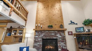 A loft-style living room with a fireplace, wooden ceiling, and a mezzanine level.