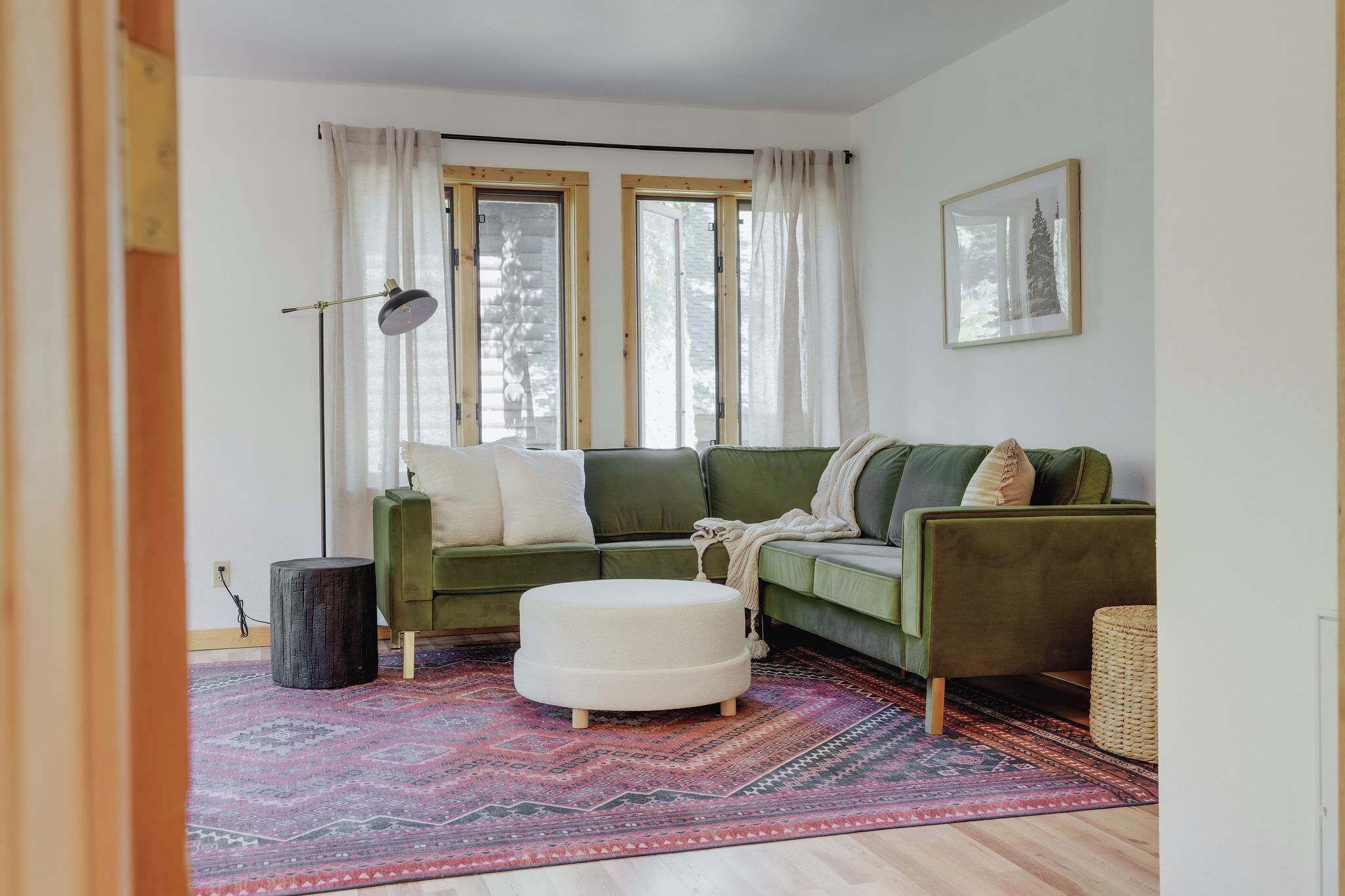 Ett vardagsrum med en grön soffa, en vit pall, en mönstrad matta och en golvlampa.
