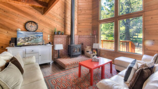 Interior acogedor de una cabaña con chimenea, ventanas amplias, un armario blanco y una zona de estar confortable.