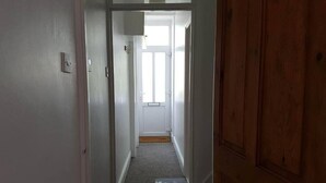 Um corredor estreito com piso coberto por carpete, um tapete de boas-vindas e uma porta de madeira à direita.