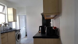 Uma cozinha compacta com máquina de lavar, cafeteira e micro-ondas.