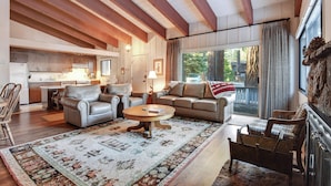 A spacious living room with a fireplace, a large window with curtains, and a kitchen in the background. - Waters Edge Escape | Patio w/ BBQ, Near Beach (Tahoma)