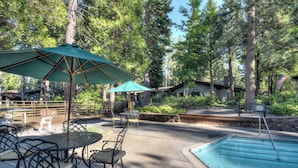 An outdoor pool area with a table and chairs, surrounded by trees and a wooden building. - Waters Edge Escape | Patio w/ BBQ, Near Beach (Tahoma)