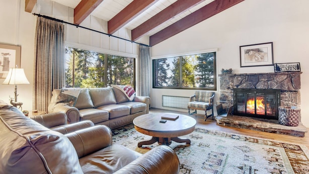 A cozy living room with leather sofas, a fireplace, and large windows offering a view of trees. - Waters Edge Escape | Patio w/ BBQ, Near Beach (Tahoma)