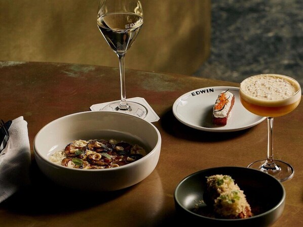 Una mesa con un bol de comida, un plato de postre, una copa de vino y un cóctel.