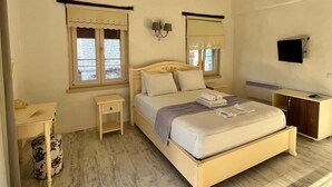 A bedroom with a large bed, a desk, a chair, a nightstand, a lamp, and a TV.
