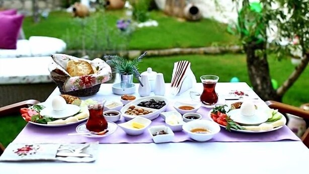 A table set for a meal with various dishes and drinks, surrounded by a garden with a stone wall and greenery.