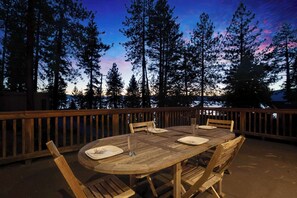 An outdoor wooden deck with a round table and chairs, surrounded by tall trees and a wooden railing. - Mountainside Overlook | Lake Views, Tree House & Hot Tub (Kings Beach)