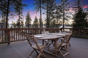 An outdoor wooden deck with a round table and chairs, surrounded by tall trees and a wooden railing. - Mountainside Overlook | Lake Views, Tree House & Hot Tub (Kings Beach)