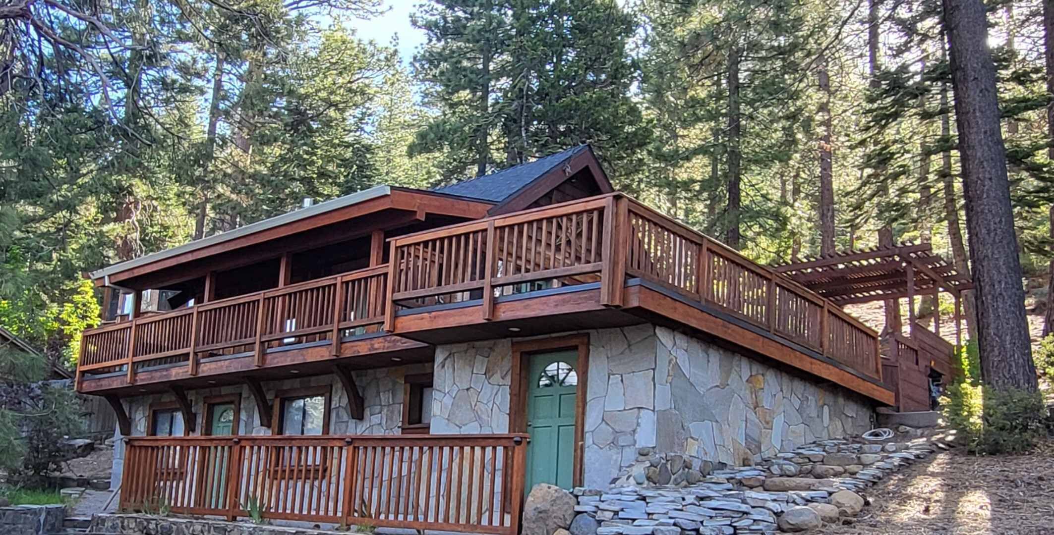 A two-story log cabin with a stone foundation, wooden balconies, and a stone entrance.
