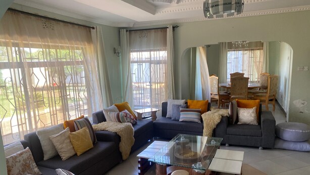 A spacious living room with a sectional sofa, a glass coffee table, and a dining area with wooden chairs and a table. - anna's homestay (Arusha)