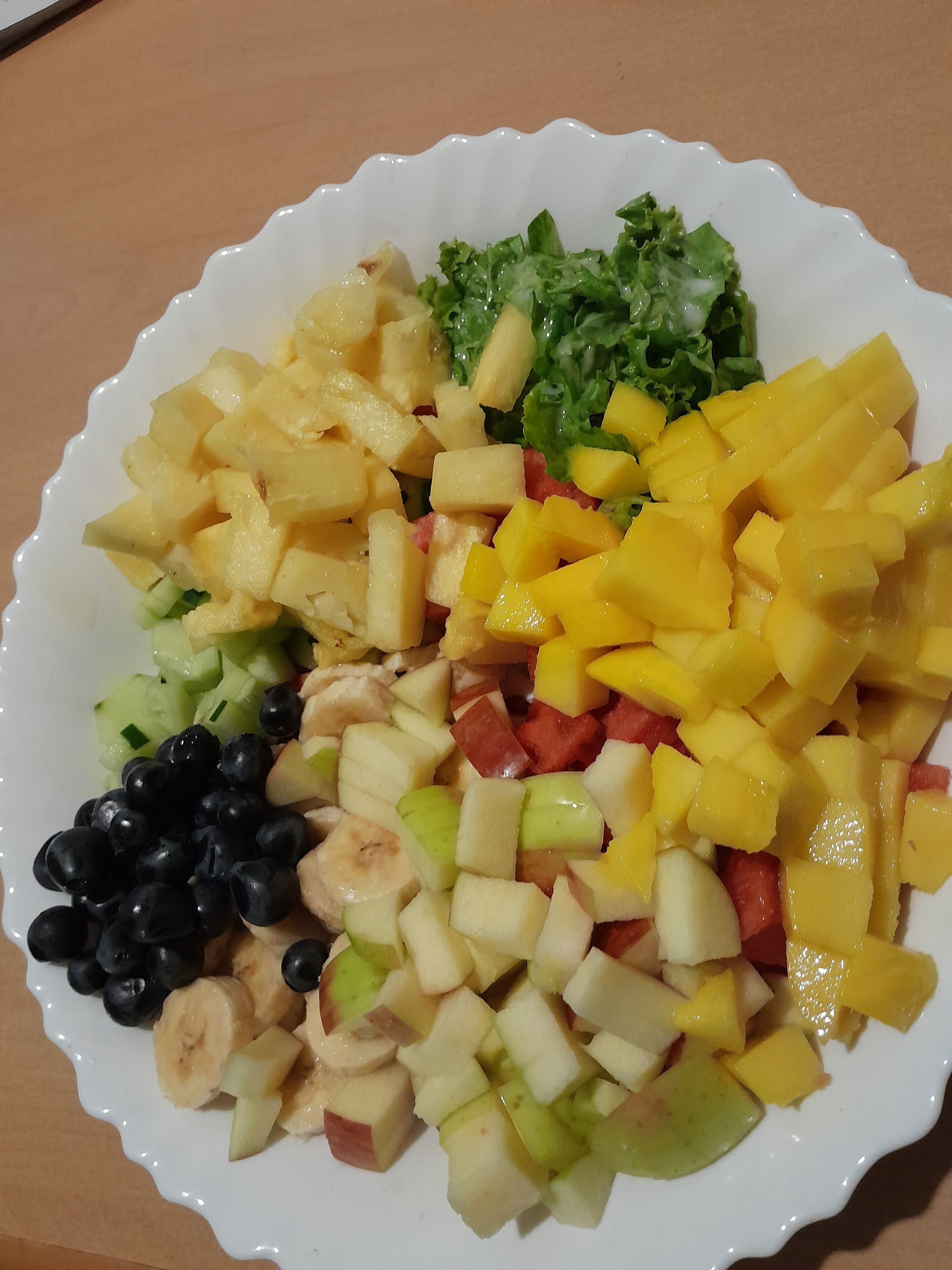 Une assiette blanche contenant une variété de fruits, notamment des pommes, des bananes et des mangues.
