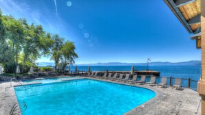 Ein rechteckiger Swimmingpool mit klarem, blauem Wasser, umgeben von Liegestühlen und Sonnenschirmen, mit Blick auf das Meer und die Berge im Hintergrund.