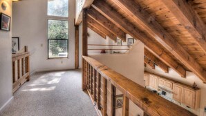 A spacious room with a high ceiling, wooden beams, a staircase, and large windows allowing natural light. - Glacier Forest Getaway | HOA Access! (Truckee)