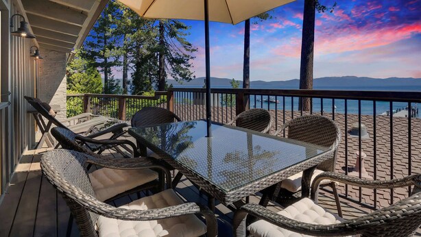 Una terraza con mobiliario de mimbre y una mesa de vidrio, con vista a un paisaje pintoresco de un lago y montañas.