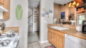 A kitchen with a stove, sink, and wooden cabinets. There is a staircase leading to another level.