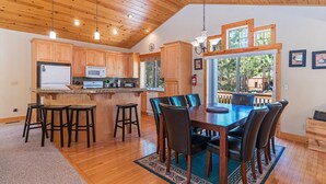 Una cocina amplia con armarios de madera y una isla grande, un comedor con mesa y sillas de madera, y ventanas grandes con vistas al exterior.