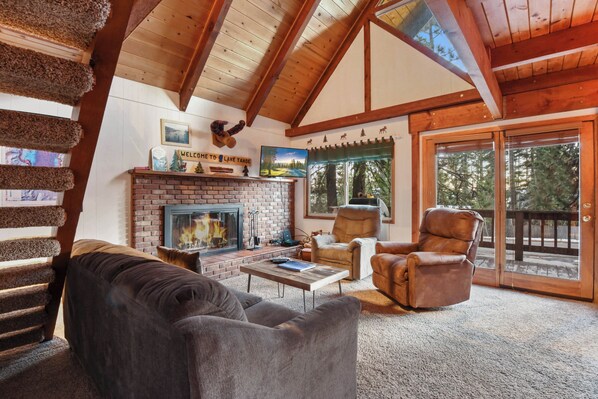 A log cabin interior with a fireplace, leather chairs, and a view of the outdoors.