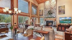 A spacious living room with a stone fireplace, large windows, and a chandelier.