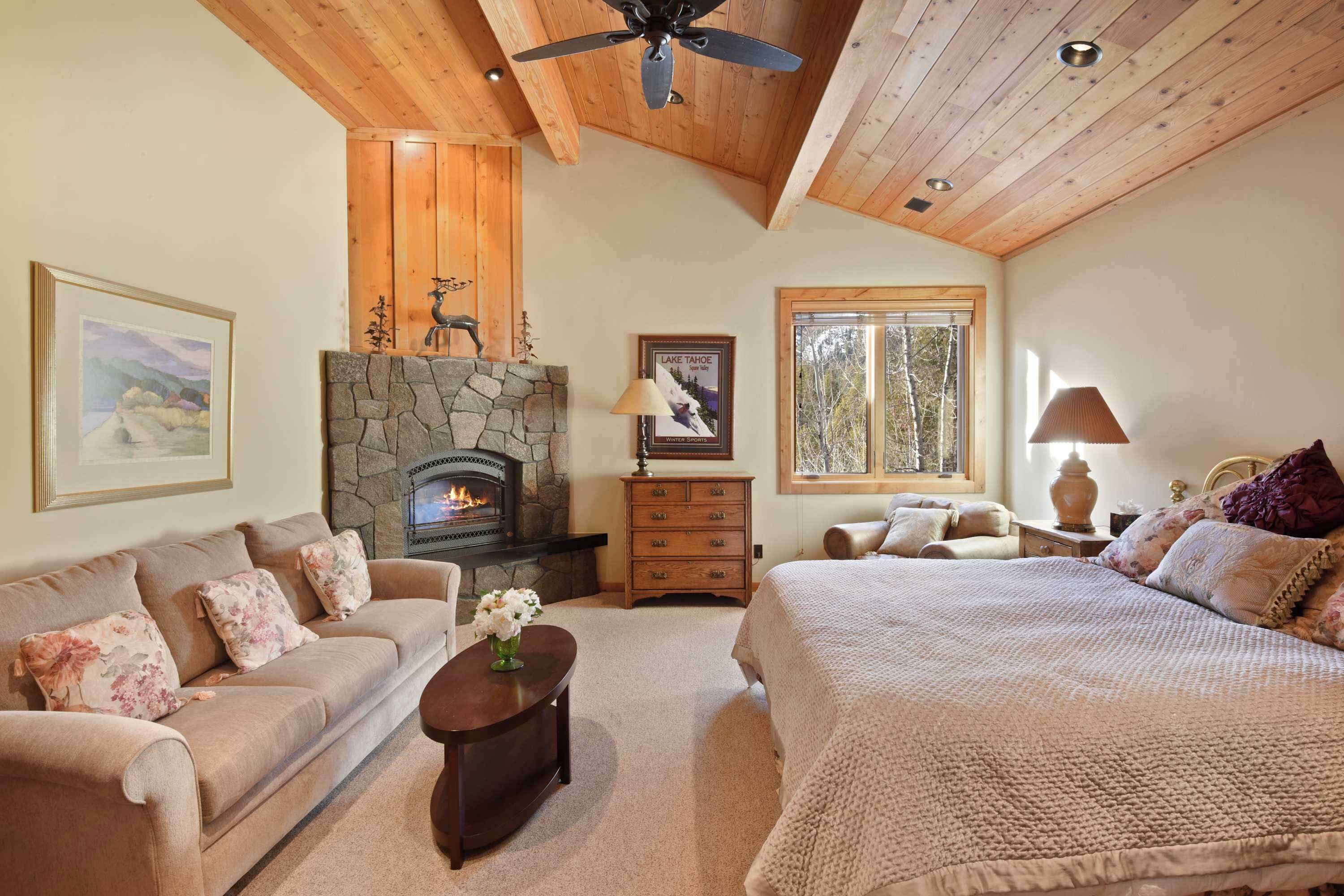 A cozy room with a stone fireplace, a bed, a sofa, and a wooden ceiling.