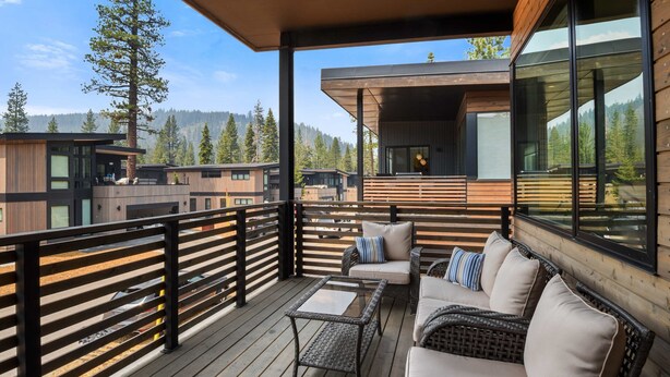 Una terraza moderna al aire libre con un sofá, sillas y una mesa, con vista a un área boscosa.
