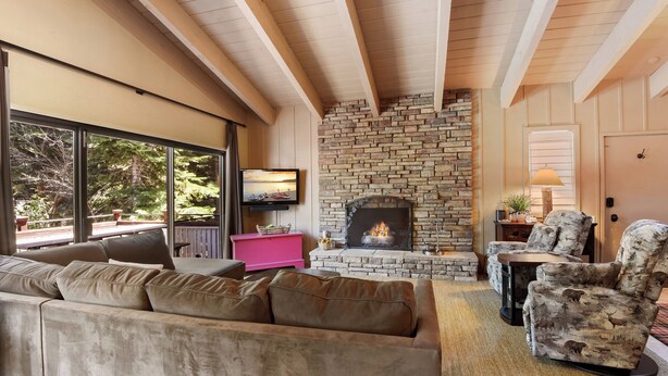 A cozy living room with a stone fireplace, a large window, and a comfortable sofa. - Waters Edge Oasis | Shared Pool & Pier Access (Tahoma)
