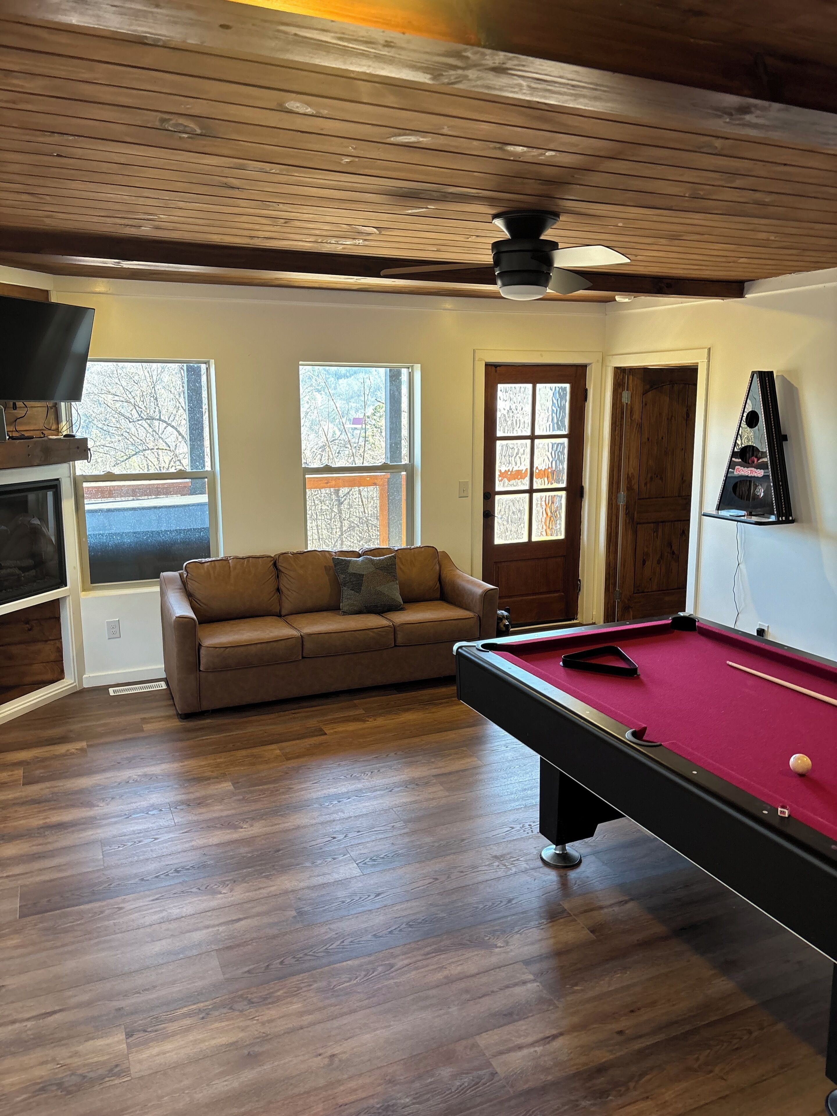 A room with a pool table, a brown leather sofa, and a television on a wooden shelf.