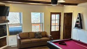 A room with a pool table, a brown leather sofa, and a television on a wooden shelf. - Home Sweet Home (Sevierville)