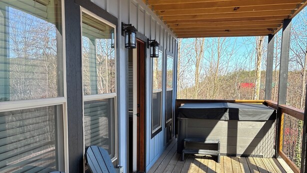 A covered deck with Adirondack chairs, a grill, and large windows overlooking a wooded area. - Home Sweet Home (Sevierville)