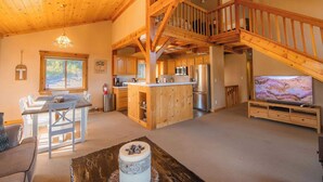 Un espacio habitable amplio con una escalera de madera, una cocina con electrodomésticos modernos y un televisor de pantalla plana grande.