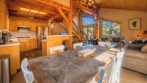 Una cocina amplia con armarios de madera y una isla grande, un área de estar acogedora con un sofá y una chimenea, y una escalera que lleva a un nivel superior.