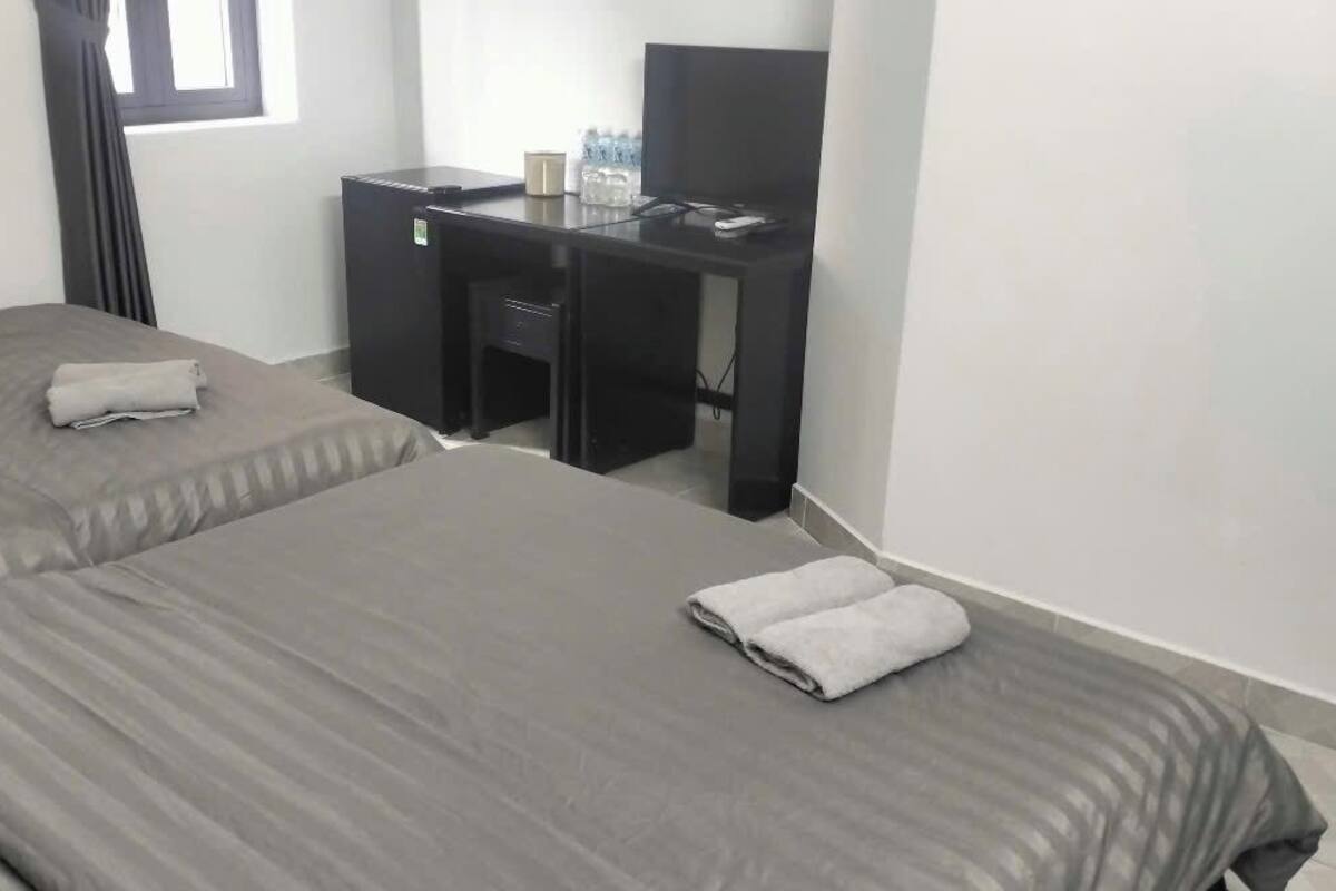 Quarto de hotel com duas camas, uma escrivaninha e uma janela.